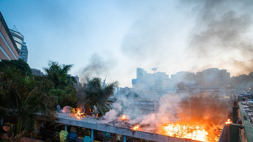 Fires burn on a building with people holding umbrellas out on one of the levels