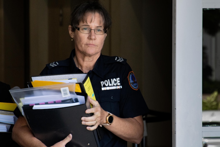 A middle-aged policewoman with brown hair carries folders leaving the court
