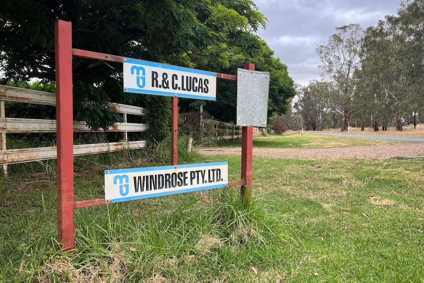 An Entrance sign to a farm by a dirt road