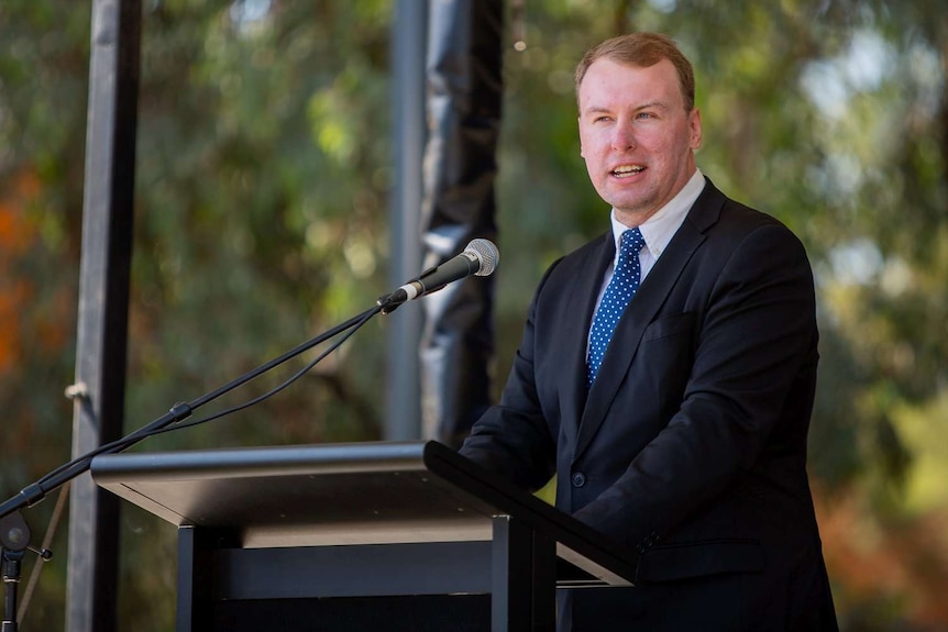 A man in a suit speaks at a lectern.