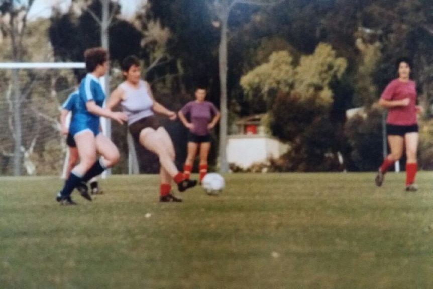 Female soccer players wearing purple, red and blue play a game