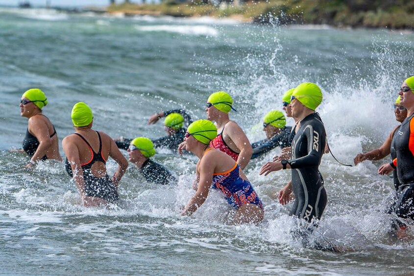 A group of women swimming in the ocean wearing fluro yellow swim caps.