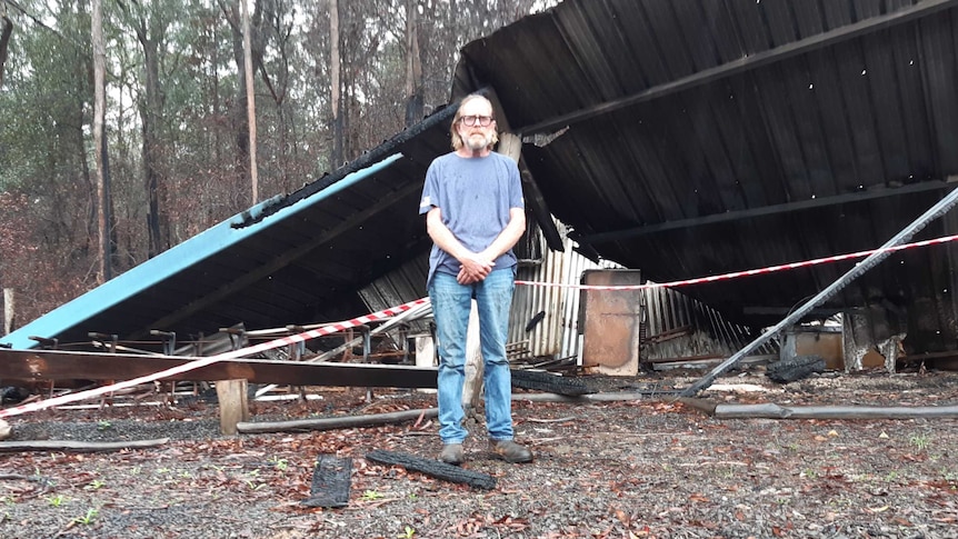 Man stands among the ruins and rubble of bushfire-destroyed property