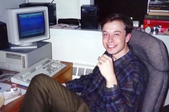 Un joven Elon Musk sonriente en una computadora de escritorio