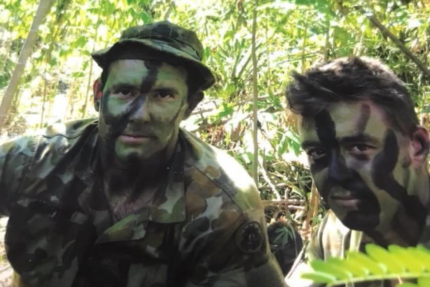 Two young men with faces painted in camoflage in the bush.