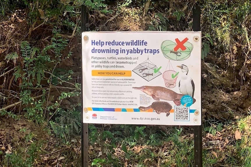 White sign with bushland in background saying 'Help reduce wildlife drowning in yabby traps'