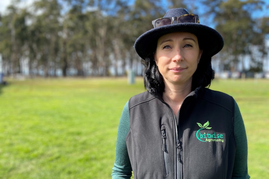 A young and proud woman stands in a field with a broad brimmed hat.