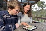 Jonty Dalton and Lucy Smith sit at a wooden table, looking at an iPad.