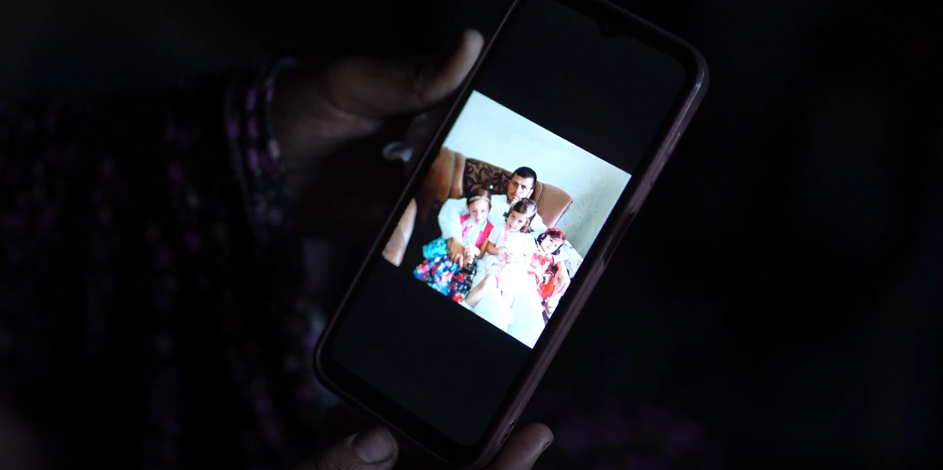 A woman shows a photo of a family on her mobile screen 