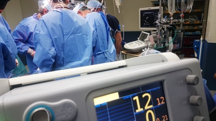 Five doctors standing around a patient during surgery, with medical equipment in the foreground.