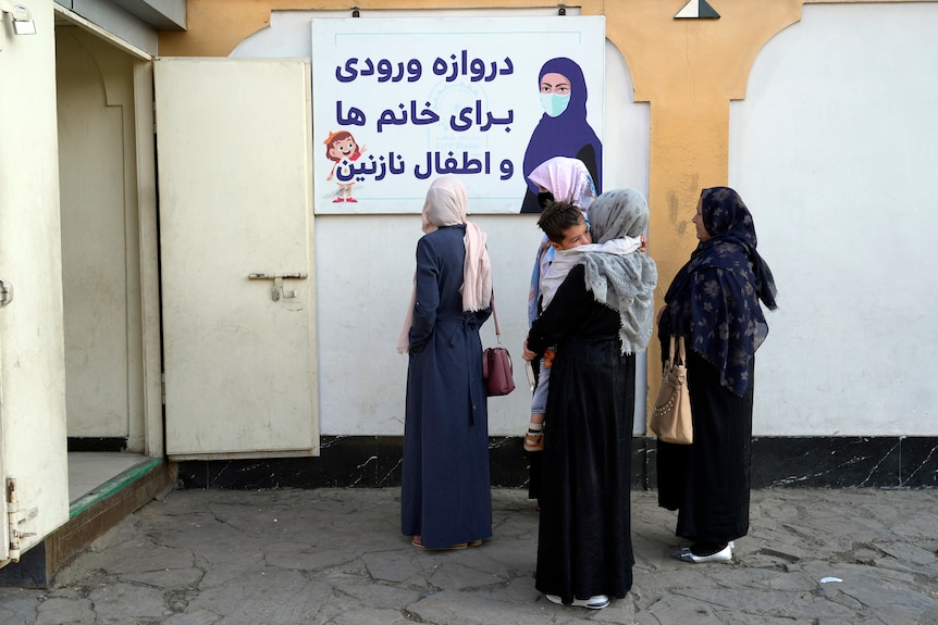 Afghan women stand outside an amusement park wearing body-covering outfits enforced by the Taliban.