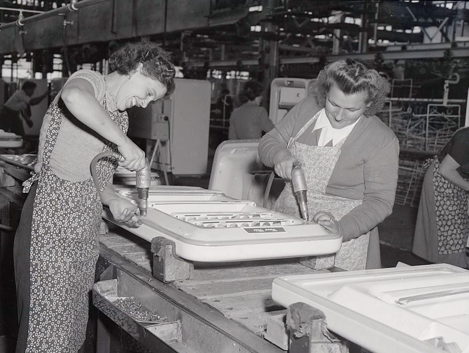 A black and white photo of two women drilling into fridge doors in the Emmco factory in 1956.