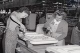 A black and white photo of two women drilling into fridge doors in the Emmco factory in 1956.