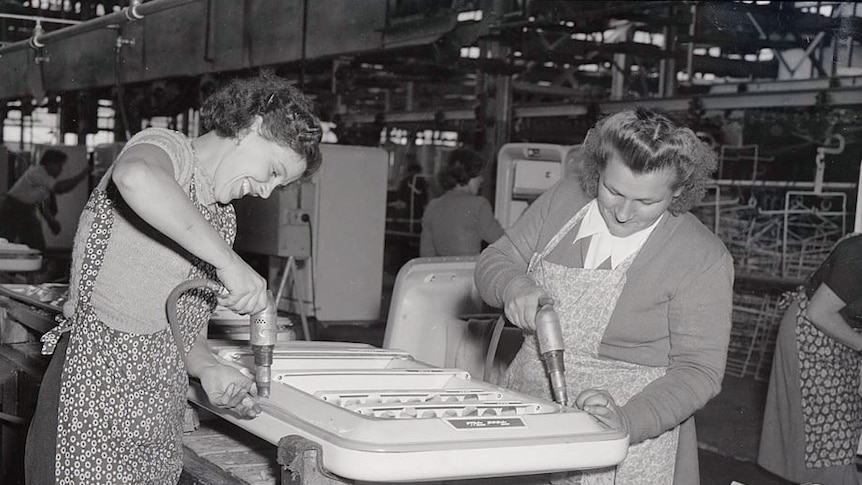 A black and white photo of two women drilling into fridge doors in the Emmco factory in 1956.