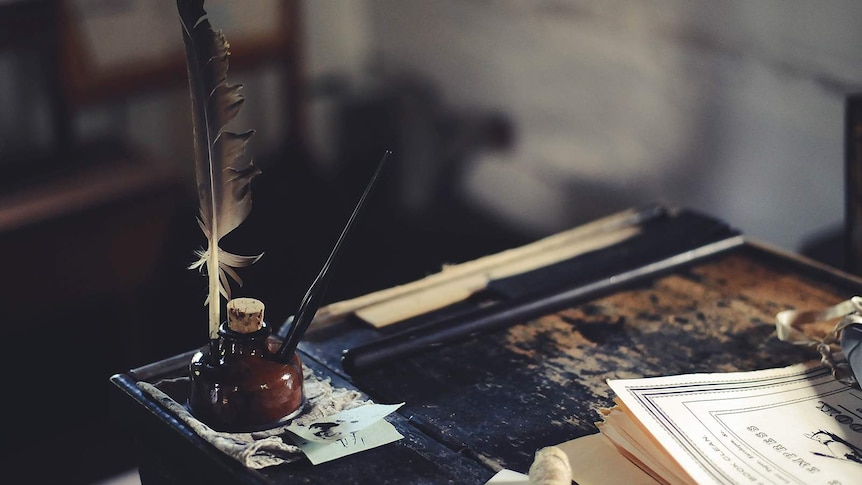 An old fashioned quill and ink set sits on a desk