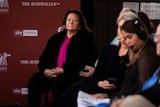 A woman sits watching a speaker intently at a conference.