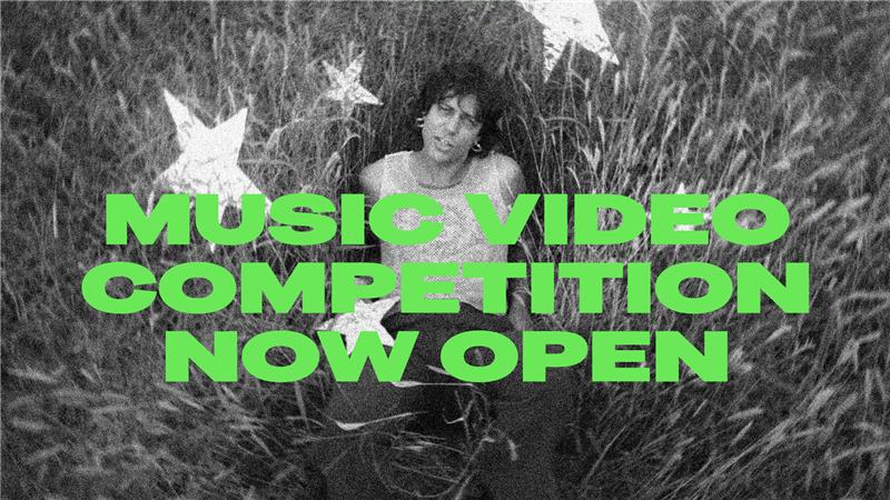 Black and white image of a man laying in grass looking up at the camera. Text overlay: Music video competition now open