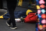 A homeless person is seen asleep in a sleeping bag on a footpath.