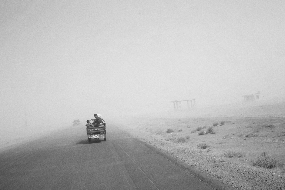 A family rides through a dust storm in the back of a rickshaw just beyond the border with Iran after being deported.