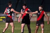 Three men wearing red and black football guernseys with two reaching out to high-five one another.