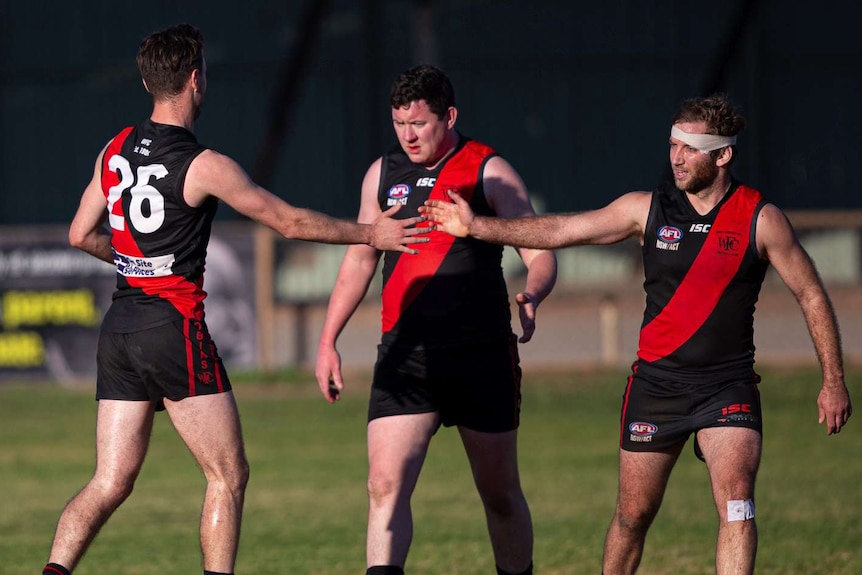 three men wearing red and black football guernseys with two reaching out to high-five one another