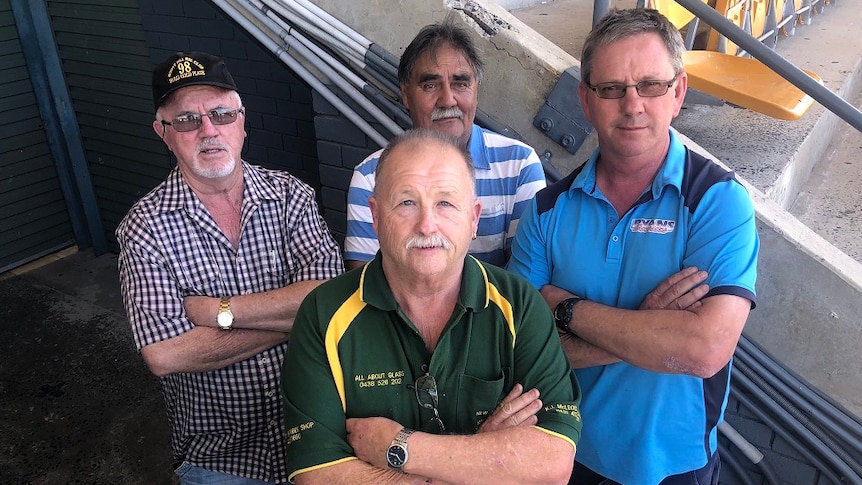 Four greyhound trainers stand with their arms crossed, not looking too happy
