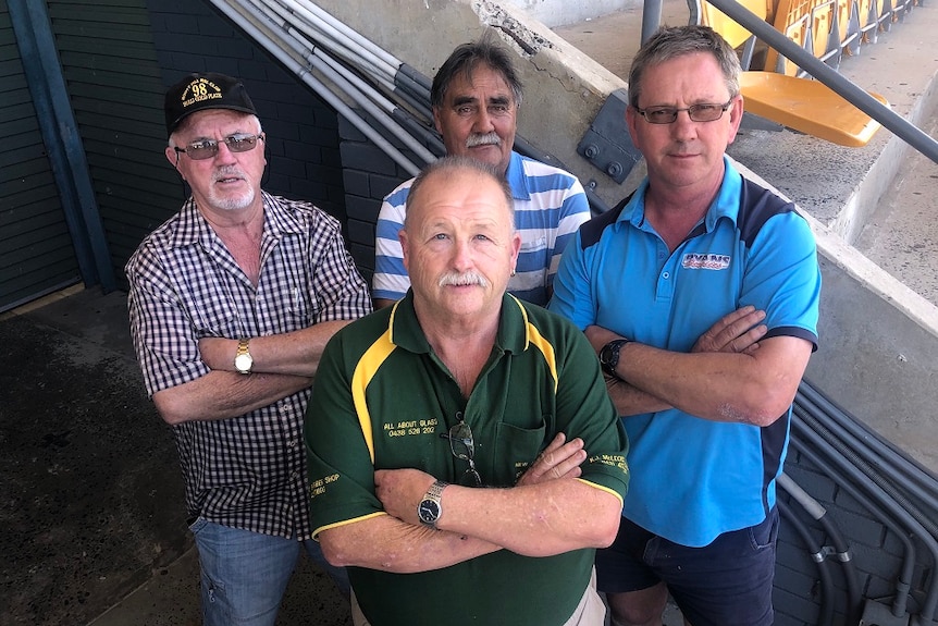 Four greyhound trainers stand with their arms crossed, not looking too happy