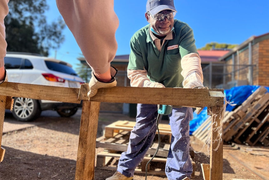 A man with a power tool cutting up wooden pallets. 