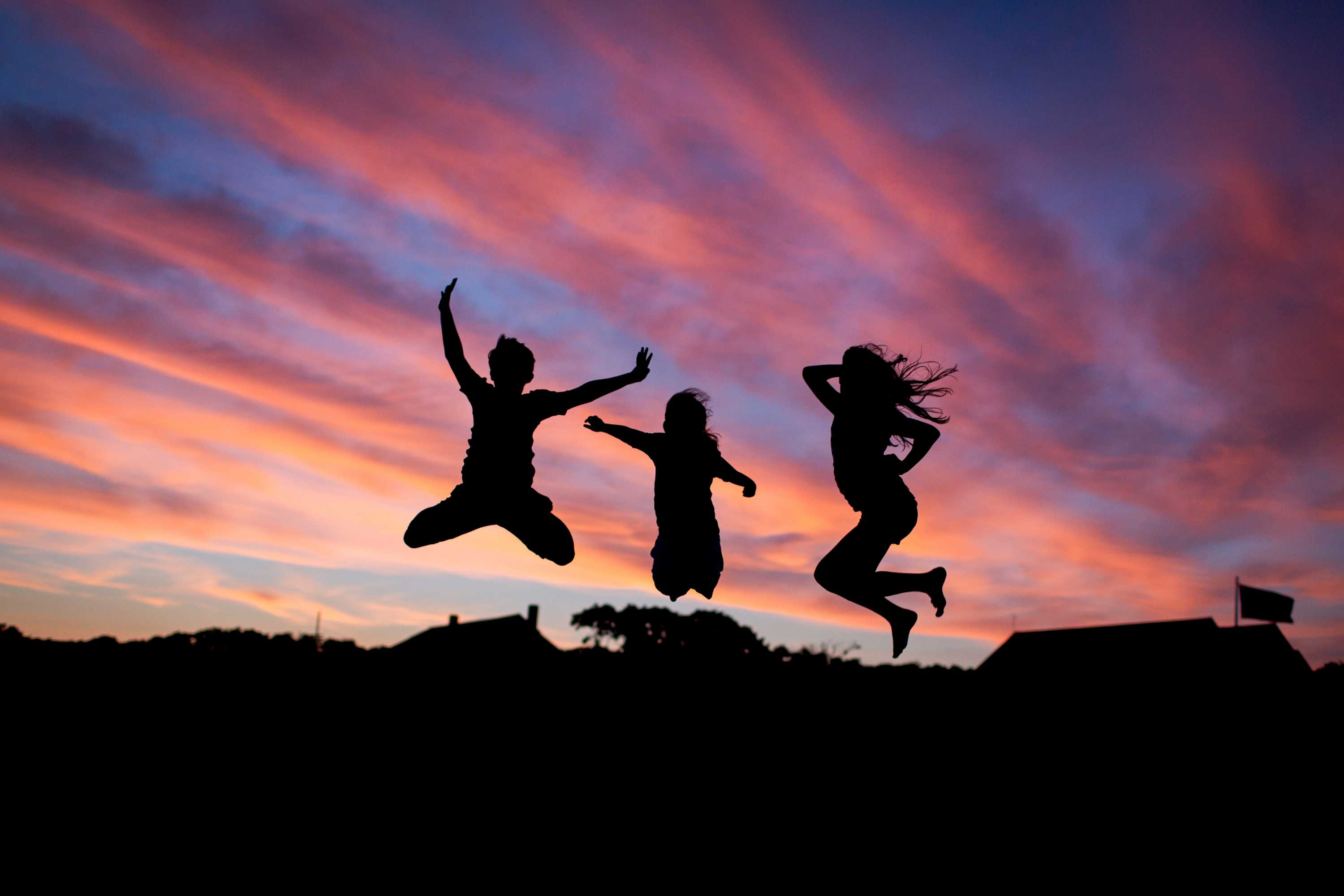 Children jumping in the air silhouetted by a vibrant pink and purple sunset