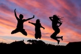 Children jumping in the air silhouetted by a vibrant pink and purple sunset