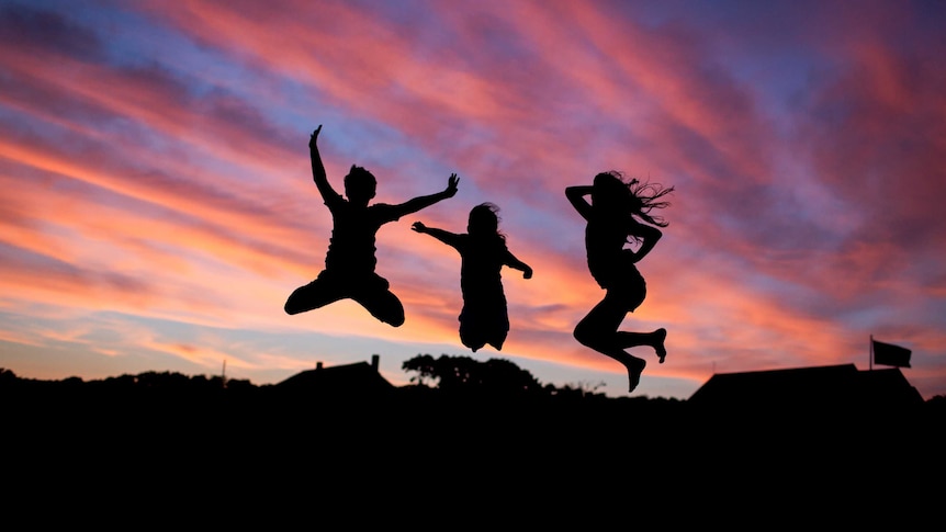Children jumping in the air silhouetted by a vibrant pink and purple sunset