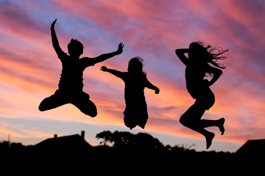 Silhouettes of happy children playing and jumping into the air at sunset.