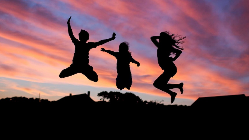 Silhouettes of happy children playing and jumping into the air at sunset.