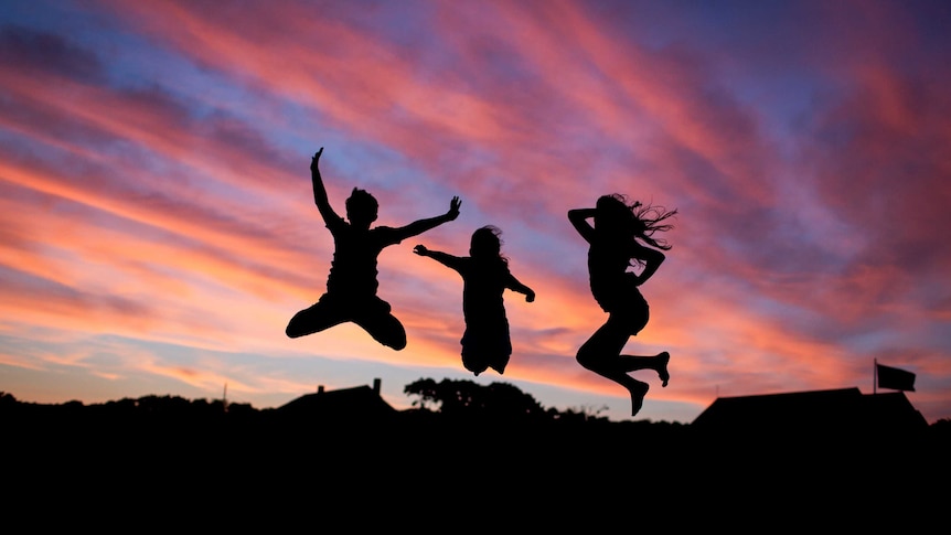 Silhouettes of happy children playing and jumping into the air at sunset.