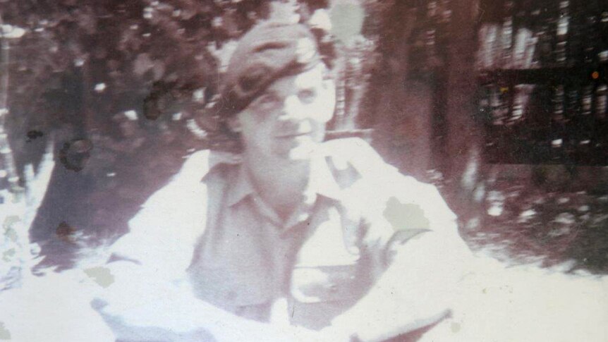 An old black and white photo of a young man in military uniform and beret, sitting casually on the ground