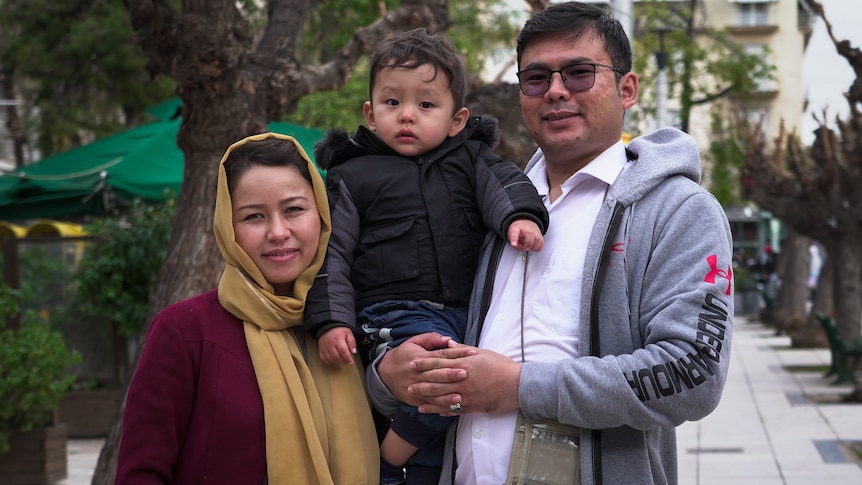 A woman wearing a red shirt with yellow hijab is standing next to a man holding a boy.