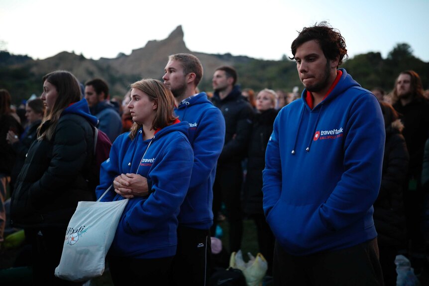 Young people wearing matching blue hoodies stand reflect in a crowd at the Gallipoli dawn service.