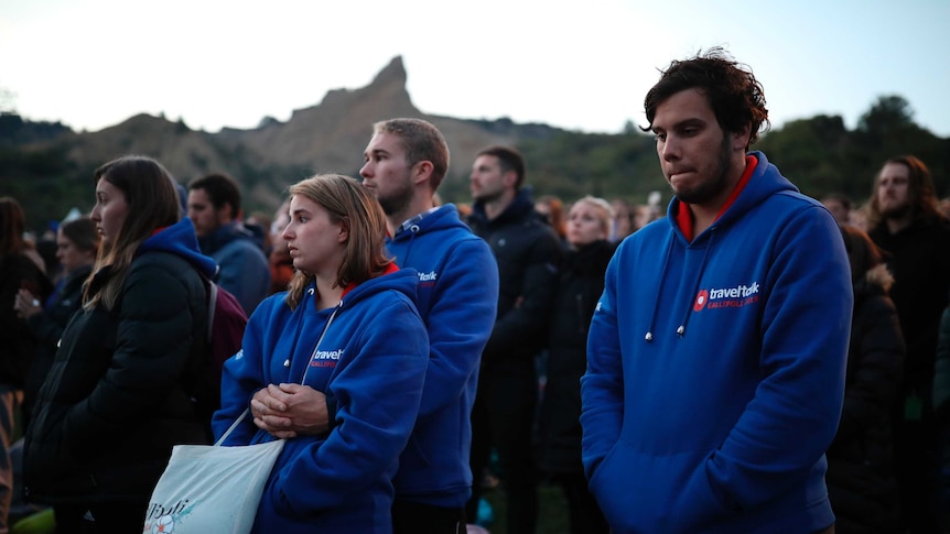 Young people wearing matching blue hoodies stand reflect in a crowd at the Gallipoli dawn service.