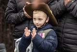 A small boy wearing a warm coat and medals stands among adults, watching the march.