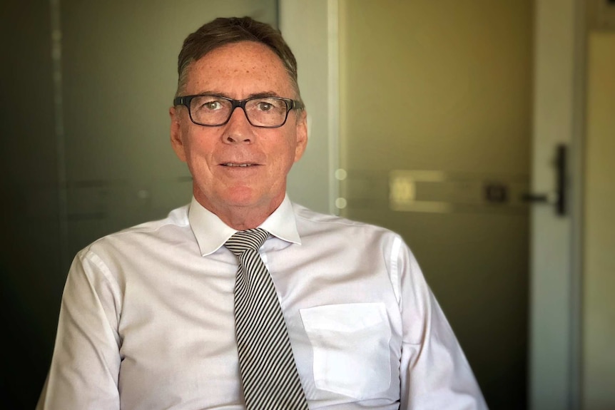 Terry Mills wears a white shirt and a tie and looks into the camera with a serious expression