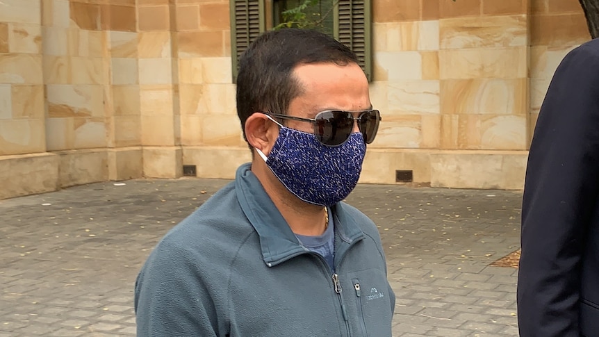 A man with short dark hair wearing sunglasses and a blue spotty face mask 