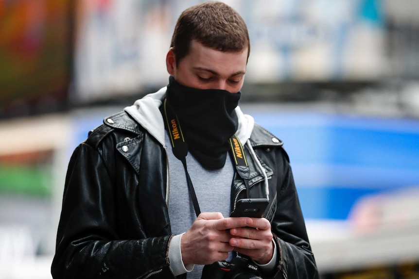 A man with a camera around his neck covers his face while looking down at his phone