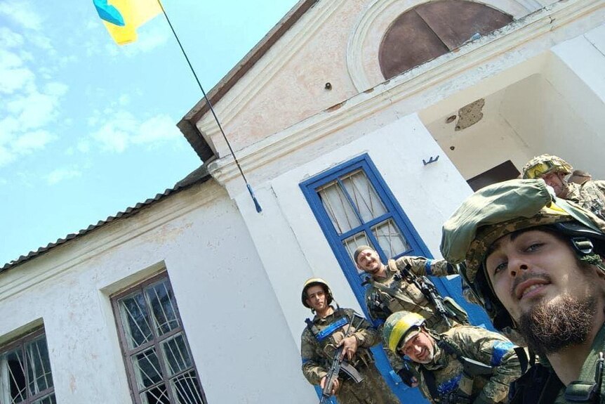 Service members pose for a picture with a Ukrainian national flag in the village of Vasylenkove.