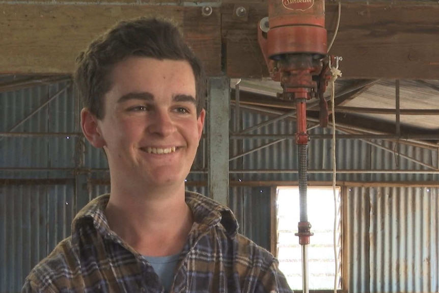 A young boy is smiling looking at the camera inside a shearing shed