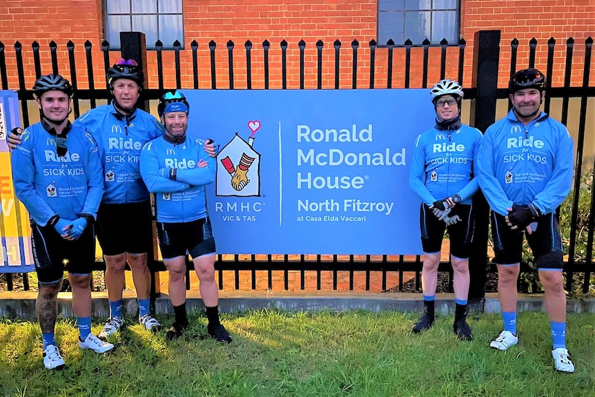 Five cyclists in blue standing outside the Ronald McDonald House in Adelaide.