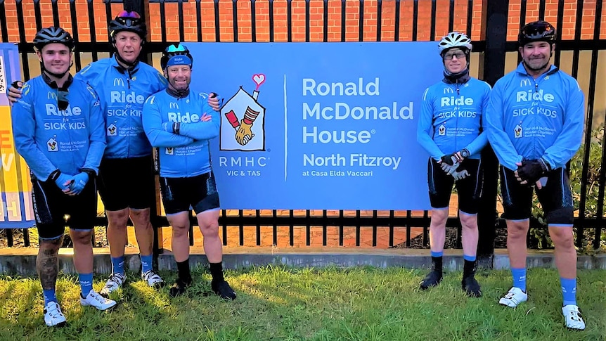 Five cyclists in blue standing outside the Ronald McDonald House in Adelaide.