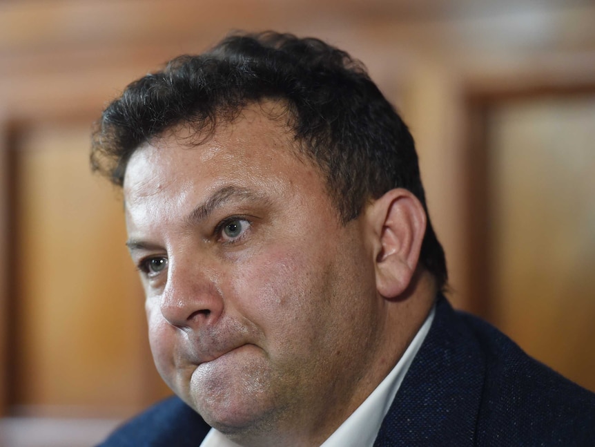 A middle-aged man with short hair looks serious as he appears at a press conference.