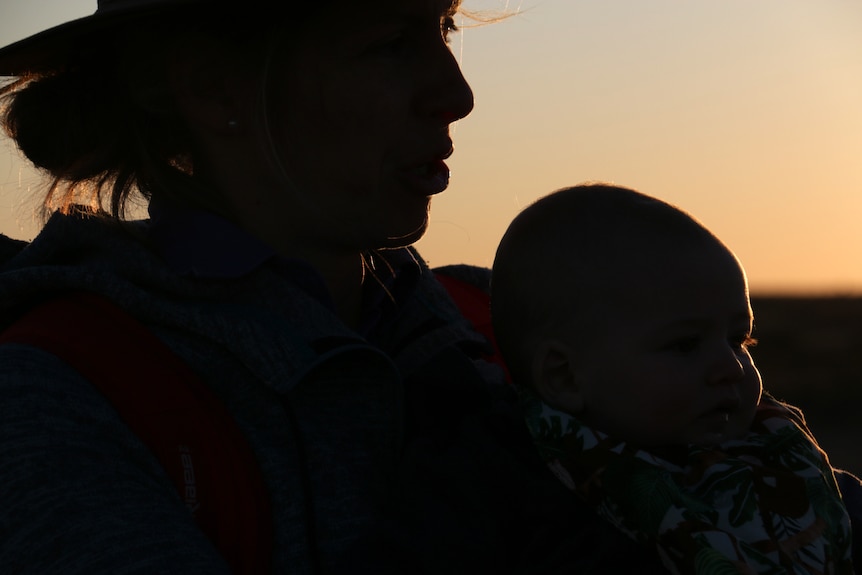 Silhouette of a woan holding a baby against a burnt orange sunset