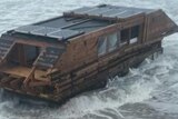 A caravan-shaped wooden boat sits on rocky beach.