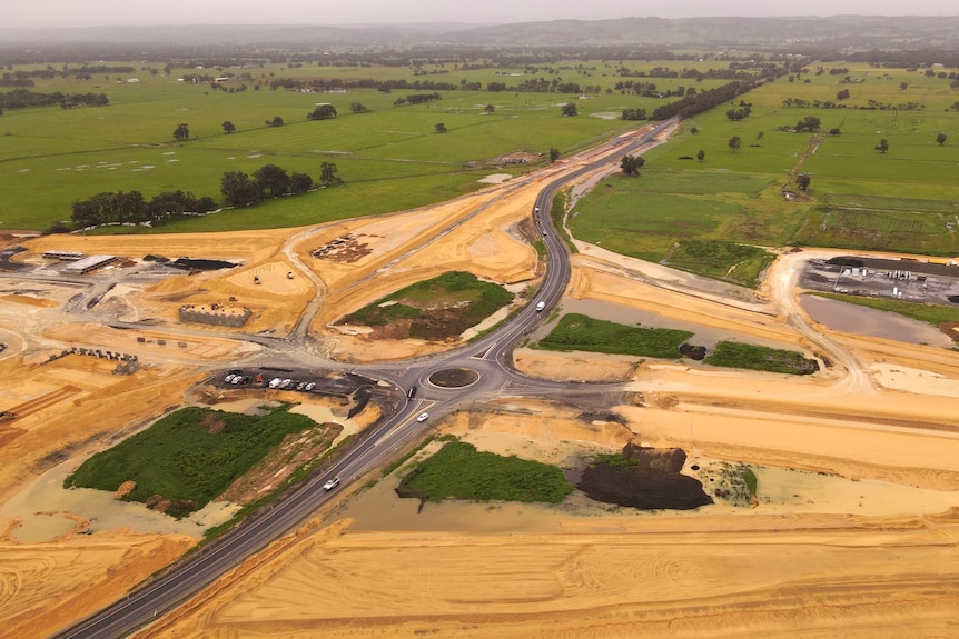 A drone shot of a road being built through green paddocks